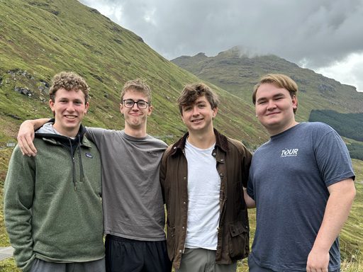 Four men taking a group photo in front of some hills