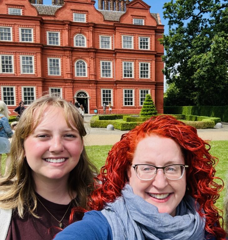 Two white women stand in front of a red brick building for a selfie.
