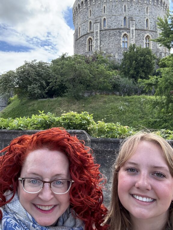 Two white women stand outside a round castle tower.