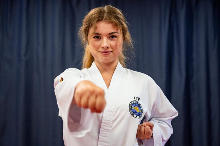 A young white woman with long brown hair smiles and holds a tae kwon do punch